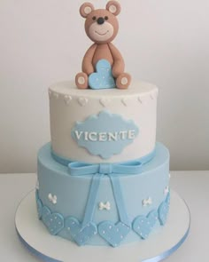 a blue and white cake with a teddy bear sitting on it's top tier