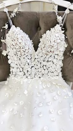 a white wedding dress with flowers on the back and straps, sitting on a couch