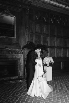 a bride and groom kissing in front of a fireplace with an umbrella over their heads