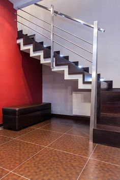 a red wall and stairs in a room with tile flooring, black bench and white handrails