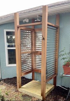 an outdoor shower with shutters on the side of a blue building and a potted plant