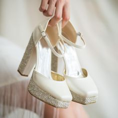 a close up of a person holding two pairs of white shoes with sparkling heels on them