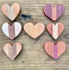 six wooden hearts are arranged on a wood surface, one is pink and the other is brown