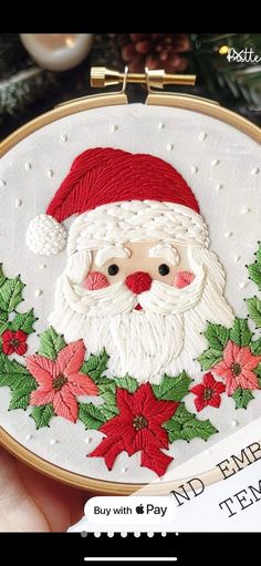 a hand embroidered santa clause with poinsettis and holly