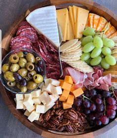 a wooden platter filled with cheese, meats, grapes and other food items