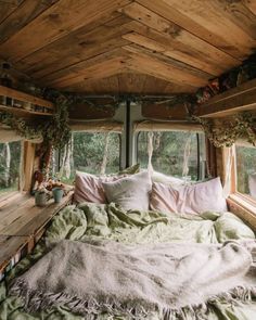 a bed sitting inside of a bedroom next to a window covered in blankets and pillows