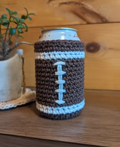 a crocheted can cooler with a football on it sitting next to a potted plant