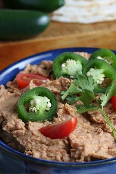 a blue bowl filled with hummus and peppers on top of a wooden table next to sliced cucumbers