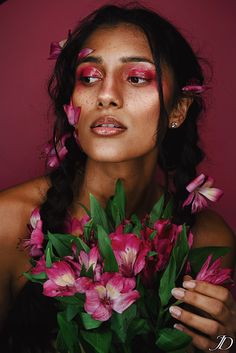 a woman with flowers in her hair and makeup is holding a bouquet of pink flowers