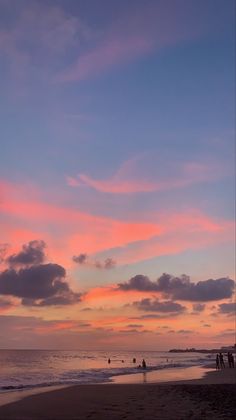 people walking on the beach at sunset with colorful clouds in the sky over the water