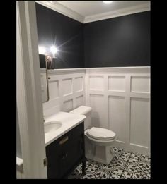 a white toilet sitting in a bathroom next to a sink under a mirror and light