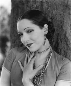 black and white photograph of a woman with necklaces on her neck posing in front of a tree