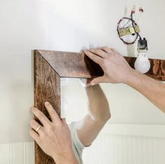 a man is working on a mirror with wood trimming around the frame and fixing it