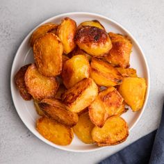 a white plate topped with fried potatoes on top of a table next to a blue napkin