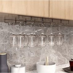 four wine glasses hanging on the wall above a counter with cups and utensils