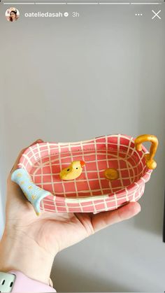 a hand holding a pink and white bowl with two little ducks in it's handles