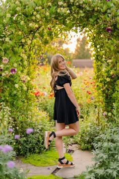 a beautiful young woman standing in front of an archway with flowers and plants around her