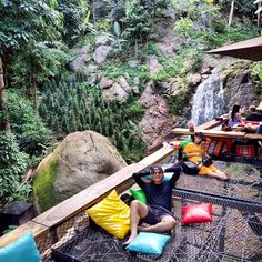 some people are sitting on the ground in front of a waterfall with lots of trees