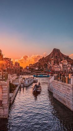 two small boats are in the water near a city with mountains and buildings at sunset