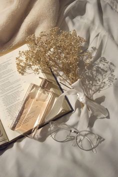 an open book and some glasses on top of a white bed sheet with a plant