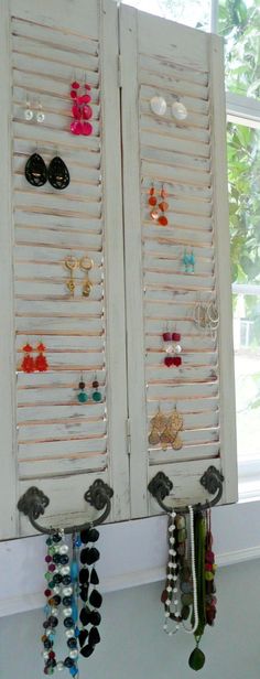 two white shutters are holding earrings and necklaces