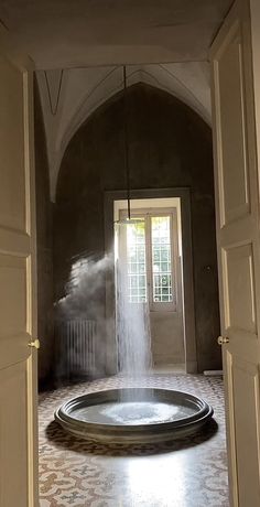 an open door leading into a room with a fountain in the center and light coming through it