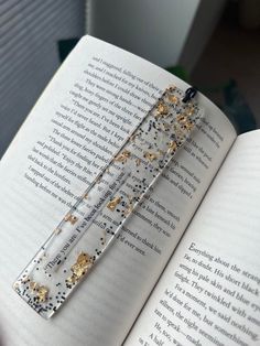 an open book with some gold and silver decorations on it's cover, sitting next to a window