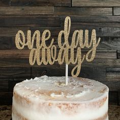 there is a cake that has the word one day on it and gold glitters