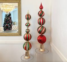 two christmas ornaments on pedestals in front of a wall with a mirror and chandelier