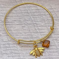 This Listing s for this Pretty Antique Gold Bee with a dainty Topaz Swarovski Crystal  on gold plated bangle Bracelet. This bracket was make with a cute double sided Antique Gold bee charm on heavy duty gold plated jump ring and a Sparkle Topaz Swarovski Crystal  (11.5mm) Princess cut pendant.  What a beautiful  bracelet to give her on her birthday. Your bracelet will come in a gift box. Thank you so much for shopping at Little Purple Lotus and supporting my small business. Any questions or conc Adjustable Gold-plated Bracelet With Charms, Adjustable Gold-plated Charm Bracelet, Adjustable Gold Plated Bracelet With Charms, Adjustable Hypoallergenic Amber Jewelry, Adjustable Yellow Gold Dangle Charm Bracelet, Adjustable Gold Bracelet With Charms For Gift, Adjustable Gold Bracelet With Charms As A Gift, Adjustable Gold-tone Charm Bracelet Gift, Amber Bangle Jewelry For Gift