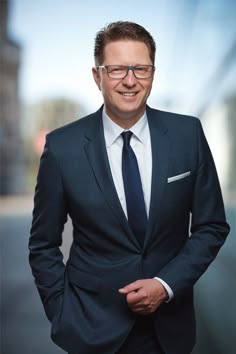 a man in a suit and tie smiling at the camera with his hands in his pockets