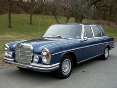 an old blue car is parked on the side of the road in front of some trees