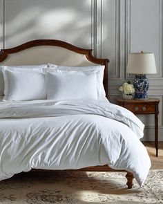 a bed with white sheets and pillows in a room next to a lamp on a table