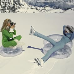 two women are sitting in the snow taking pictures