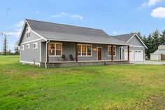 a small gray house sitting in the middle of a green field with two garages