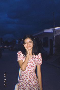 a young woman standing in the street at night with her hand on her face and looking up