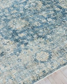 an antique rug with faded blue and beige colors on the floor in front of a wooden floor