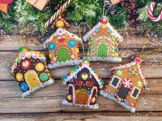 four gingerbread house ornaments on a wooden table with candy canes and christmas decorations