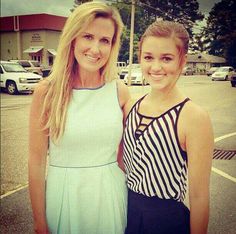 two young women standing next to each other in a parking lot with cars behind them