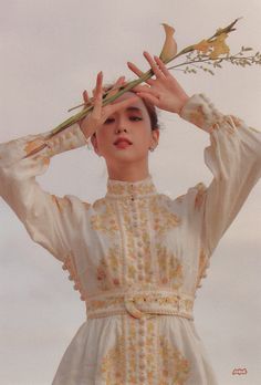 a woman in a white dress holding a branch over her head with one hand and the other above her head