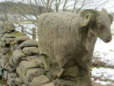 a stone sculpture of a ram next to a rock wall with snow on the ground