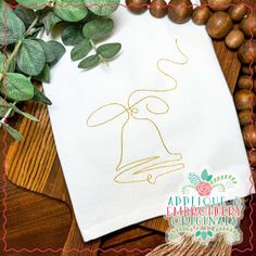 an embroidered tea towel with a bell on it, surrounded by leaves and beads in the background