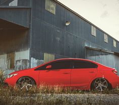 a red car is parked in front of a building with an industrial area behind it