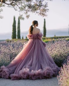 a woman in a purple dress standing under a tree with lavender flowers on the ground