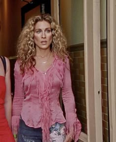 two women standing next to each other in front of a brick wall, one wearing a pink top