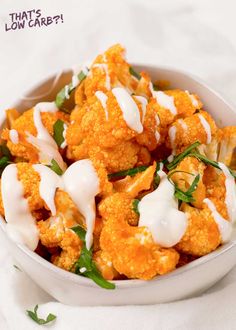 a bowl filled with cauliflower covered in white sauce and garnished with green leaves