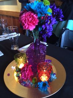 a purple vase filled with colorful flowers sitting on top of a table next to glasses