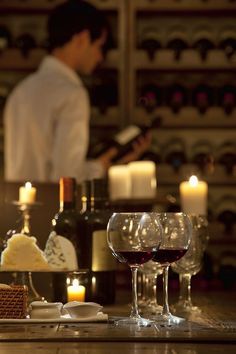 two glasses of wine are sitting on the counter next to bottles and candles in front of a chef