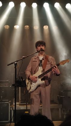 a man standing in front of a microphone while holding a guitar