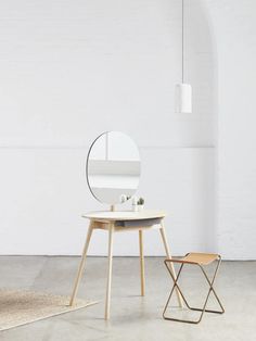 a round mirror sitting on top of a wooden table next to a stool and rug